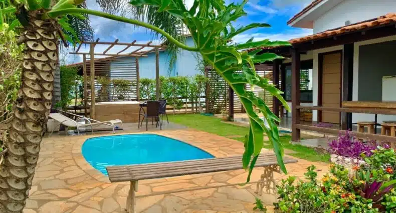 Parte externa da Casa de Temporada em Capitólio (Charme e Aconchego) com uma piscina azul em volta um piso de pedra. Há também algumas plantas verdes, algumas cadeiras e do lado direito aparece o pedaço da construção da casa. Imagem ilustrando post Airbnb em Escarpas do Lago.