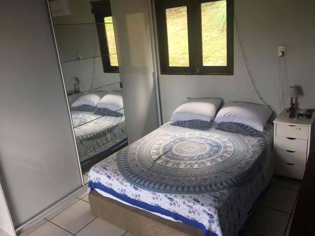 Quarto da Casa do Ney. Uma cama de casal no meio, do lado direito uma cômoda, do lado esquerdo um guarda-roupa com espelho. Em cima da cama uma janela. Foto para ilustrar post sobre airbnb em Fernando de Noronha.