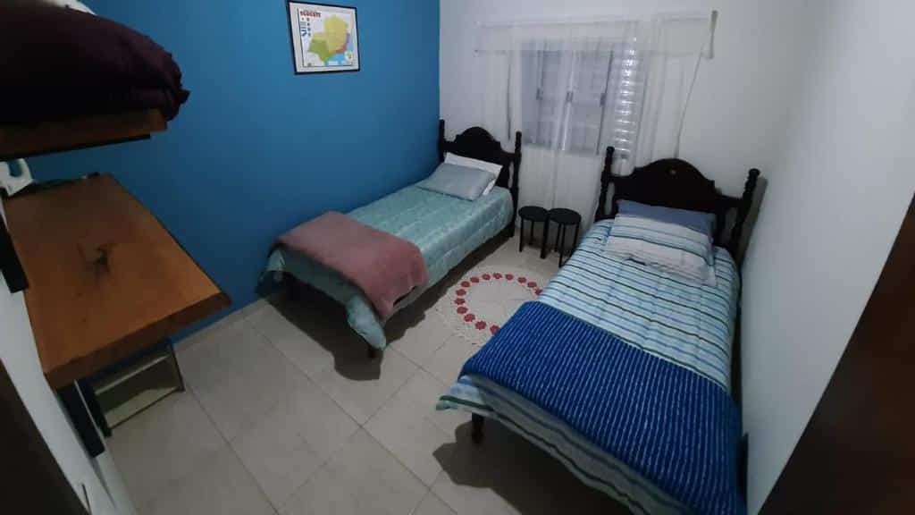 Quarto da Casa Kiiro. Duas camas de solteiro, entre elas uma janela e dois bancos. Do lado esquerdo uma prateleira. Foto para ilustrar post sobre airbnb em Santo Antônio do Pinhal.