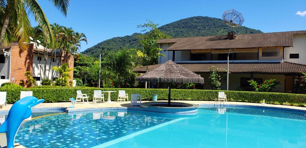 Foto da área externa da Casa Melo 4 para ilustrar post sobre airbnb em Perequê Mirim. Uma piscina com uma ilha de quiosque e cadeiras de praia ao redor. Ao redor um jardim e no fundo prédios