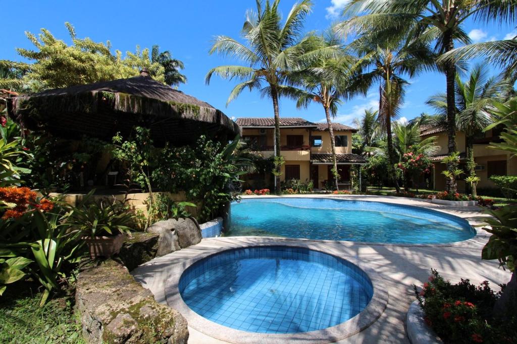 Área externa da Casa 32 Paraty. Uma piscina pequena redonda, atrás uma grande, ao redor o jardim da casa, do lado esquerdo um quiosque pequeno, no fundo a casa e palmeiras.