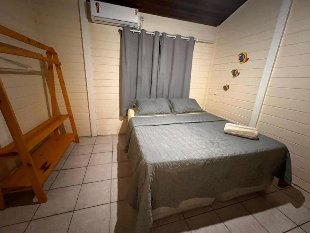 Quarto da Casa Renascer. Uma cama de casal do lado direito, do lado esquerdo uma estante de madeira. Foto para ilustrar post sobre airbnb em Fernando de Noronha.