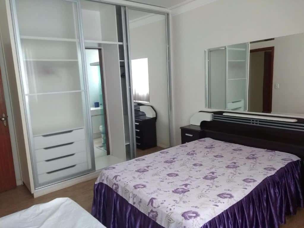 Foto do quarto da Casa verde em Belo Horizonte. Há uma cama de casal na direita, uma cabeceira atrás e um espelho. Na esquerda, há um guarda-roupa com espelho também.