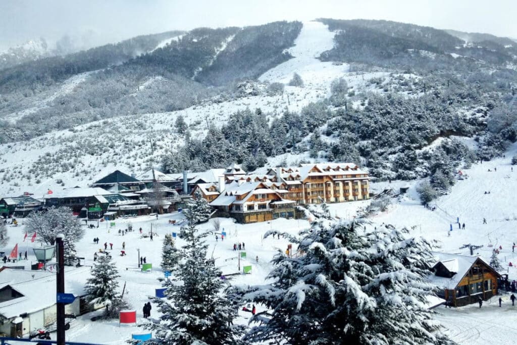 Vista do Cerro Catedral, com muita neve e pessoas esquiando. No centro uma propriedade.