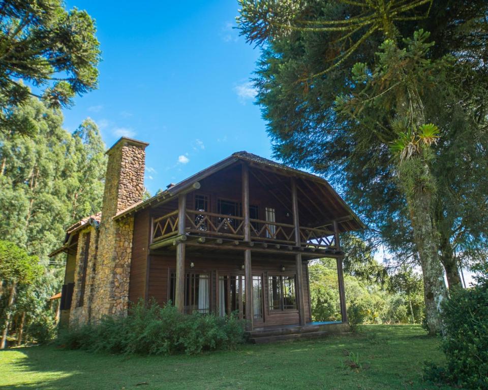 Chalé da pousada Aires de Patagonia visto de fora. O chalé é grande, tem uma estrutura de madeira e uma chaminé ao lado. As portas e janelas são de vidro e há dois andares, com uma varanda em cima. Em volta do chalé há um área verde com árvores e gramado.