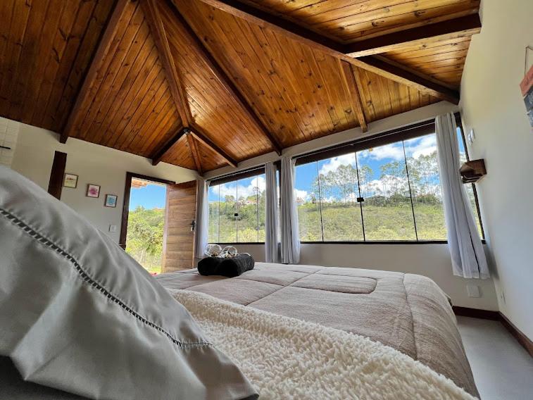Vista do quarto do Chalé do Lírio em Ouro Preto, como quem está deitado na cama. A cama é box e de casal, na frente dela há uma janela extensa com vista para o campo.