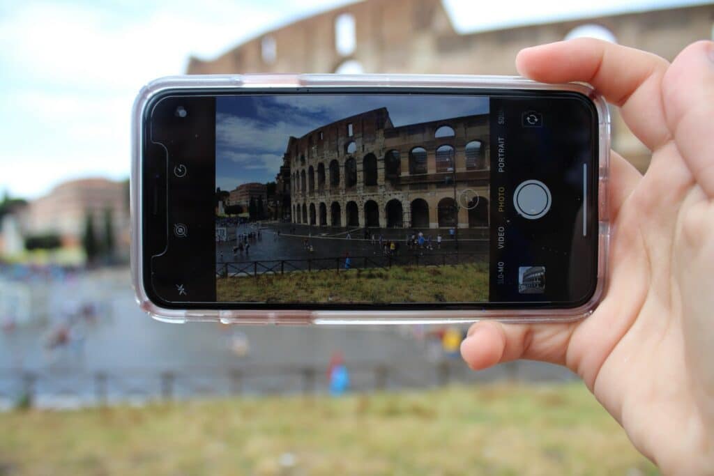 Mão branca segurando um celular tirando foto do Coliseu, em Roma, na Itália.