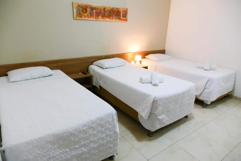 Quarto do Ecos Conforto. Três camas de solteiro, entre eles uma prateleira e em uma delas uma luminária. Foto para ilustrar post sobre hotéis em Porto Velho.