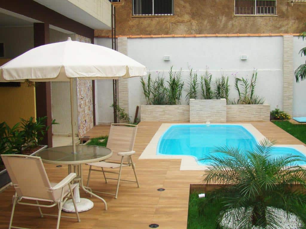 Área externa do Ecos Conforto. No lado direito uma piscina e um jardim, do lado esquerdo uma mesa com duas cadeiras e um guarda-sol.