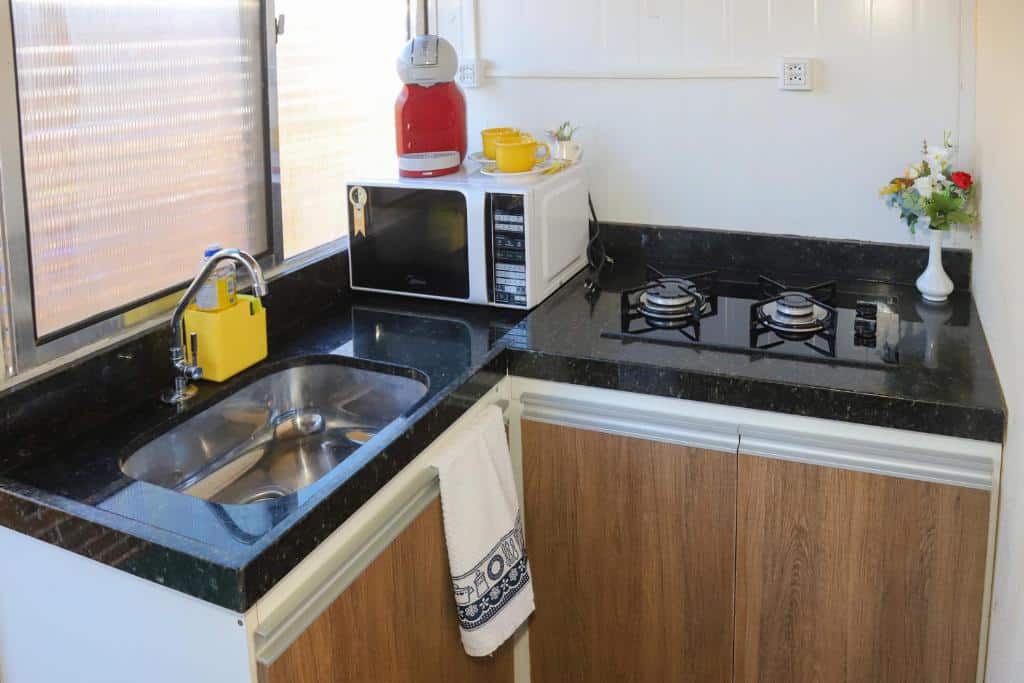 Cozinha do Flat Vista Mar Noronha. Um armário, do lado esquerdo uma pia e um micro-ondas, do lado direito um cooktop.