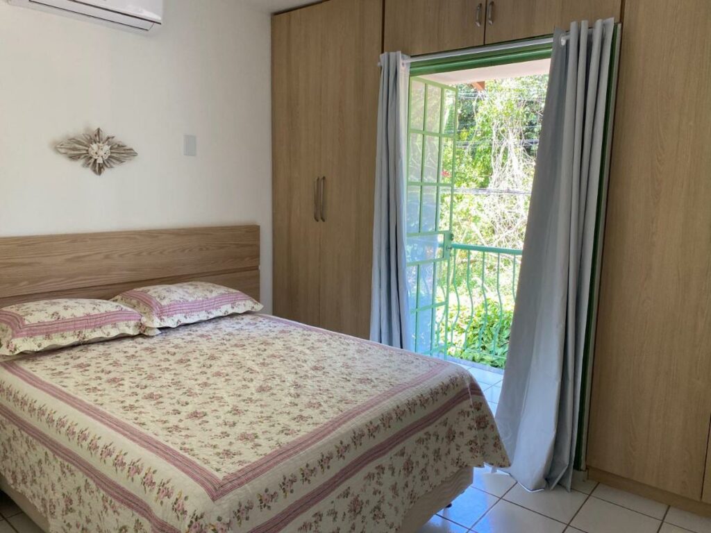 Quarto do airbnb Flores da Aldeia. Uma cama de casal está no meio do ambiente, ao lado da porta para a varanda.