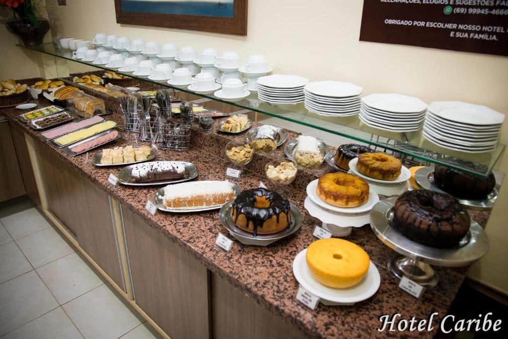 Balcão do café da manhã do Hotel Caribe. Pratos e xícaras em cima, em baixo bolos, frios e pães.