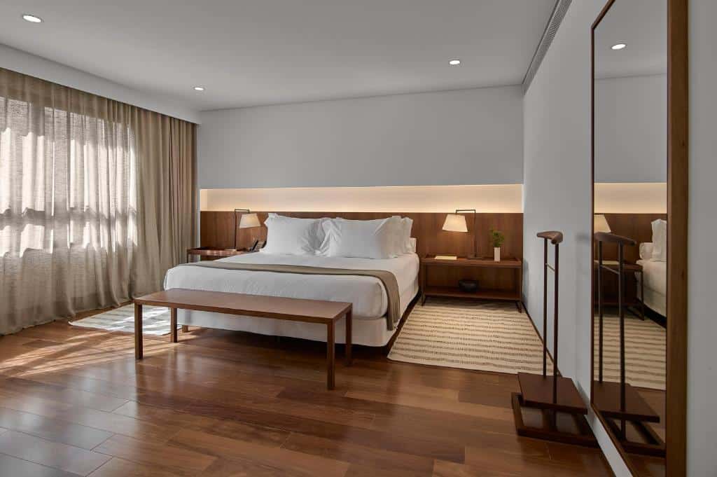 Quarto do Hotel Fasano Belo Horizonte  com cama de casal, duas cômodas ao lado da cama, janela do lado esquerdo e espelho na parede no lado direito.