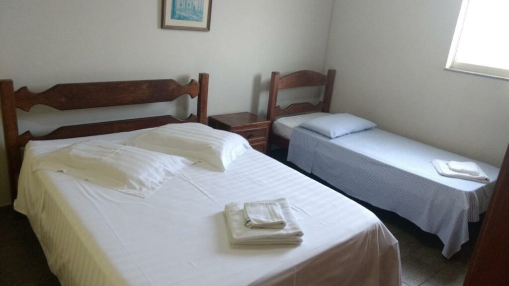 Quarto do Hotel Lund. Uma cama de casal e uma cama de solteiro estão lado a lado. Entre elas há uma mesinha pequena.