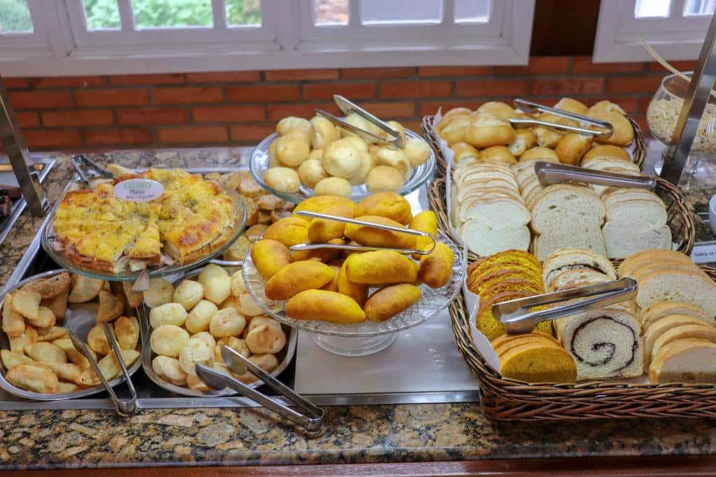 Mesa de café da manhã do Hotel Pousada Ald' Mama. Cestas com pães, bolos e tortas.