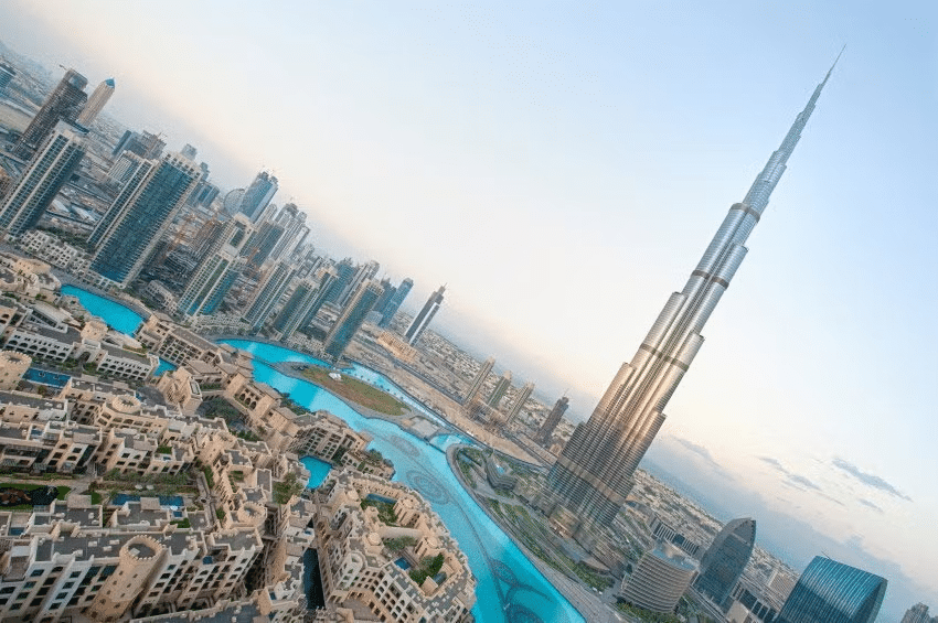 Vista de Dubai com o Burj Khalifa ao lado, ele é uma estrutura pontuda e estilosa, há lagos artificiais ao redor e prédios organizados