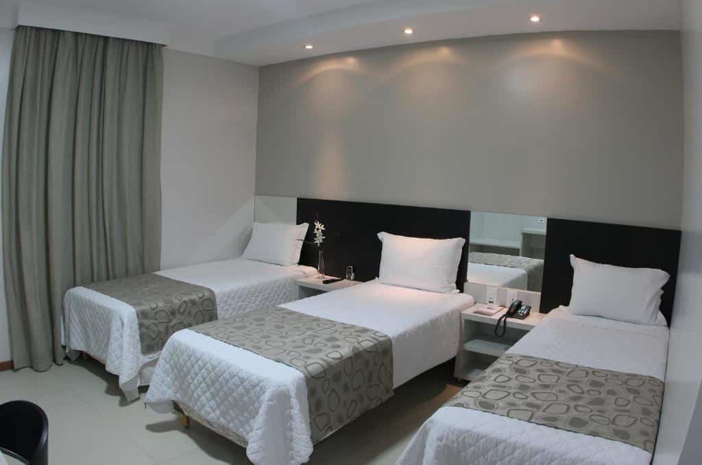 Quarto do L´acordes Hotel. Três camas de solteiro e entre eles uma cômoda. No lado esquerdo uma cortina fechada. Foto para ilustrar post sobre hotéis em Porto Velho.
