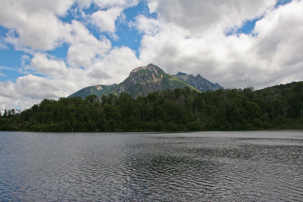 Um lago na frrente, atrás muitas árvores e a ponta de uma montanha. Imagem para ilustrar post sobre o que fazer em Bariloche.