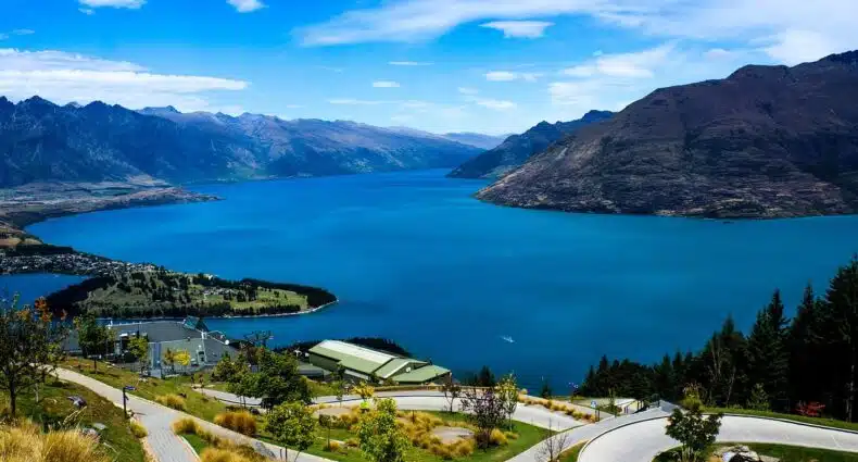 Vista da parte costeira de Queenstown, com jardins e ruas e o lago Wakatipi ao fundo com montanhas no horizonte.