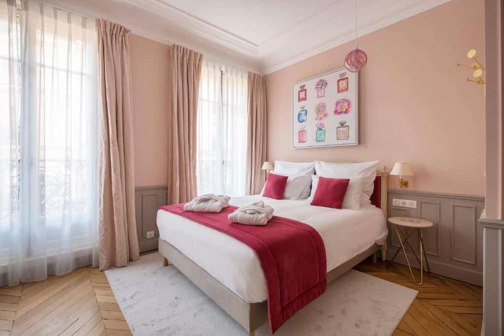 Quarto do LE BEAU MARAIS - Luxury Apartments, AIR COND, LIFT decorado em tons de rosa. Uma cama de casal com almofadas e toalhas tem mesinhas de cabeceira e abajures dos dois lados, assim como um tapete abaixo. A parede o lado esquerdo tem duas janelas com cortinas.