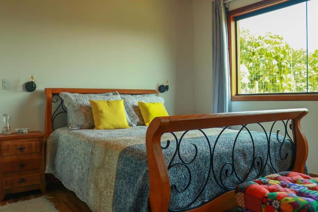 Quarto da Linda vista para as montanhas. No meio, uma cama de casal com almofadas. Do lado esquerdo uma cômoda, do lado direito a janela. Foto para ilustrar post sobre airbnb em Santo Antônio do Pinhal.