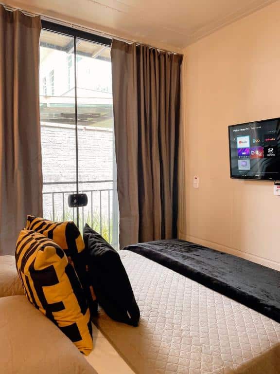 Quarto do LOFT BC. Uma cama de casal do lado esquerdo e de frente uma televisão. No fundo uma porta de vidro com cortinas abertas. Foto para ilustrar post sobre airbnb em Balneário Camboriú.