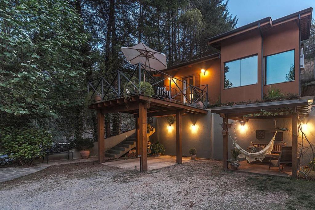 Área externa do Loft Luz. Do lado direito um deck com rede e bancos, em cima uma varanda com mesa, cadeiras e guarda-sol.