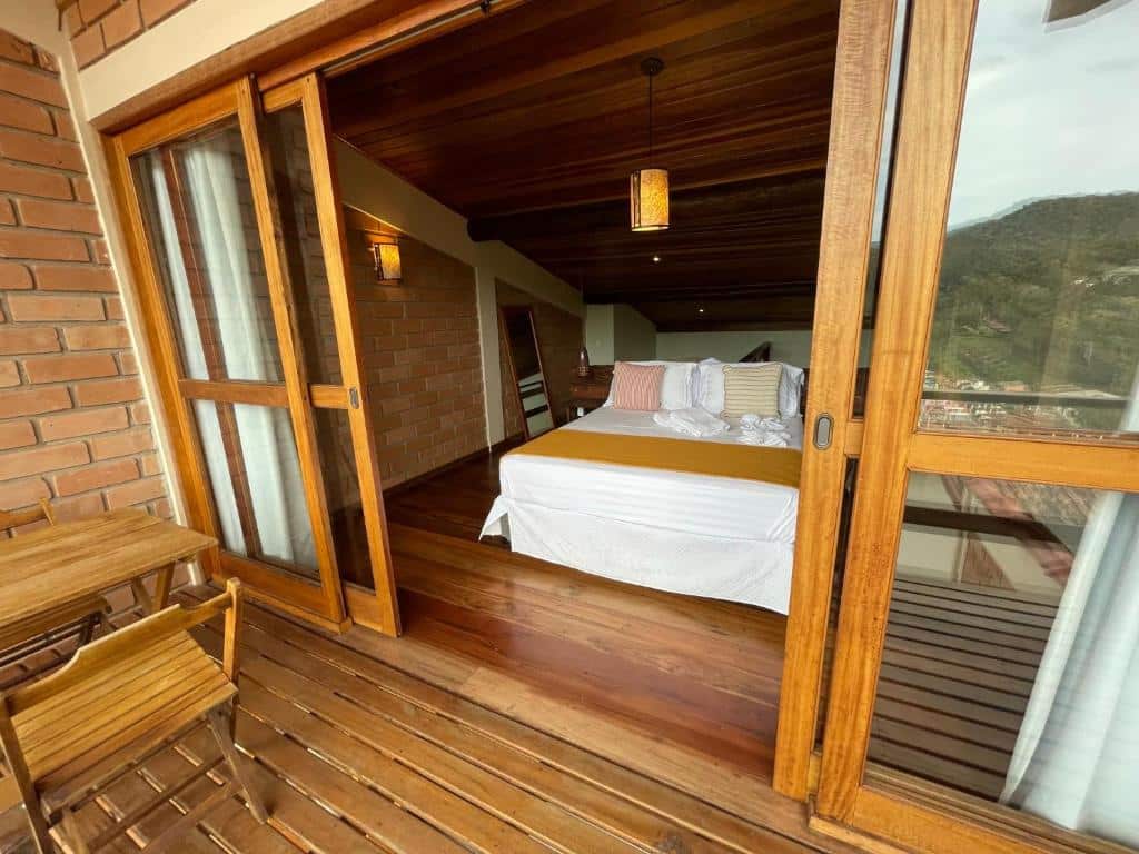 Quarto do Loft Maika'i. Uma varanda na frente com uma mesa de madeira e duas cadeiras. A porta de vidro e no fundo uma cama de casal. Foto para ilustrar post sobre airbnb em Santo Antônio do Pinhal.