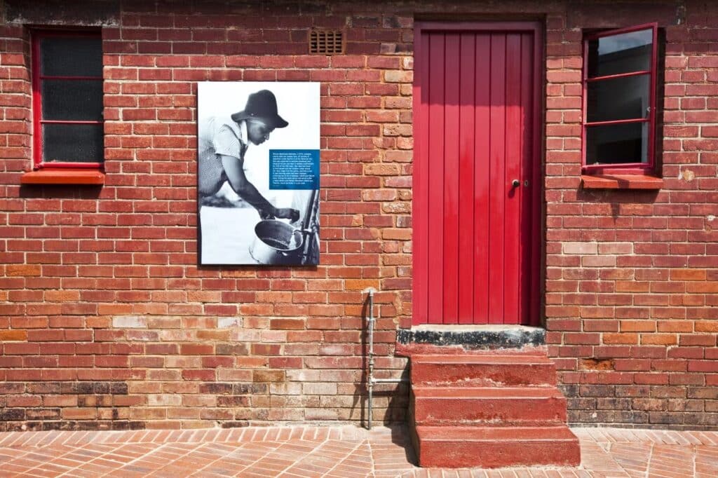 Frente de uma casa de tijolos, porta e janelas vermelhas. Três degraus levam até a porta, que fica ao lado de um quadro de Nelson Mandela mais jovem. - Foto: Civitatis