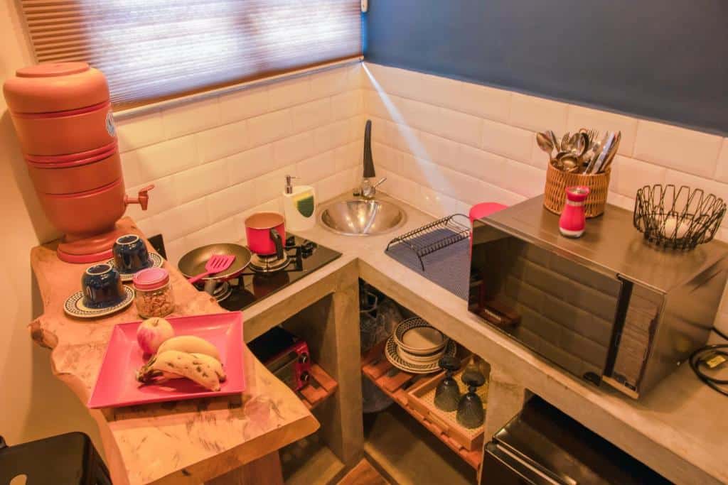Mini cozinha do Mantiqueira Flat
Do lado direito um micro-ondas com utensílios de cozinha. No meio um pequeno fogão com frigideira e leiteira, em baixo um forninho e do lado uma pia. No canto esquerdo um balcão com um filtro, xícaras e um prato com fruta.