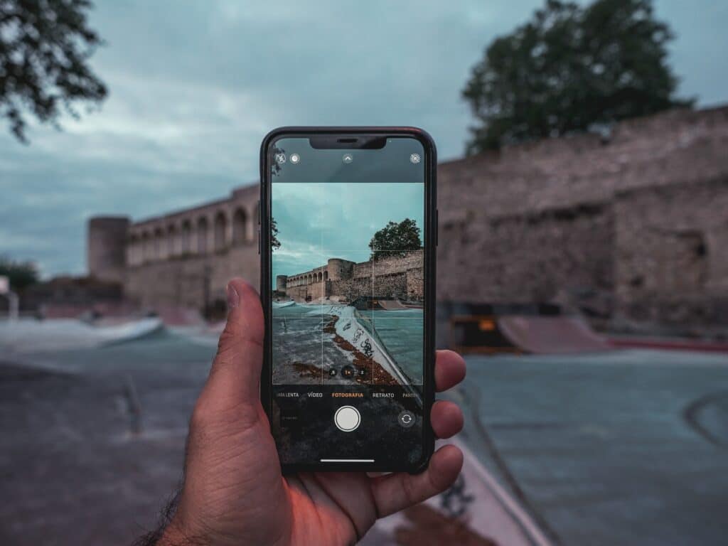 Mão esquerda masculina branca segurando um iphone para fotografar um antigo castelo de pedras de Abrantes, Portugal.