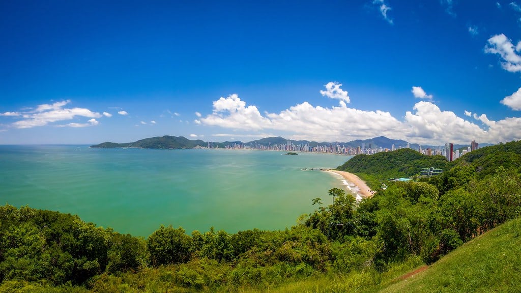 Vista do Morro do Careca. Várias árvores na frente, no fundo um mar verde cristalino. Imagem para ilustrar post sobre o que fazer em Balneário Camboriú.
