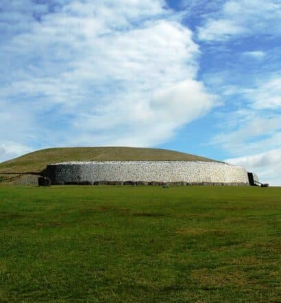 Um monumento cercado por rochas em um campo amplo e verde, para representar Newgrange na Irlanda