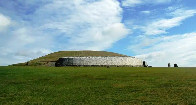 Um monumento cercado por rochas em um campo amplo e verde, para representar Newgrange na Irlanda