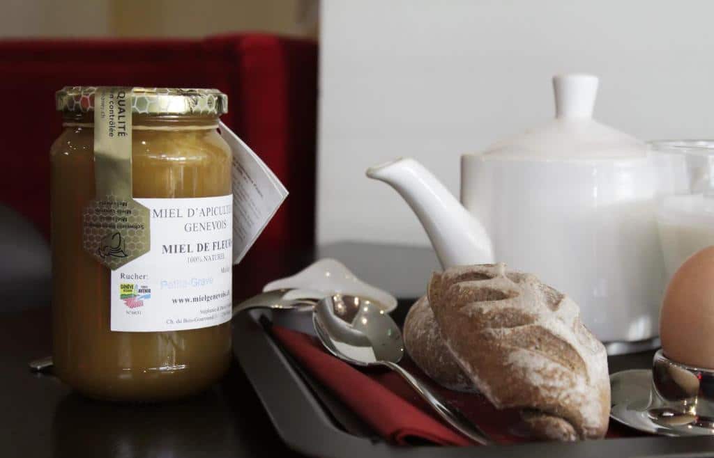 Exemplo de um café da manhã servido no N’vY Manotel. Há uma geleia de mel e uma bandeja com dices, ovo e um copo de leite.