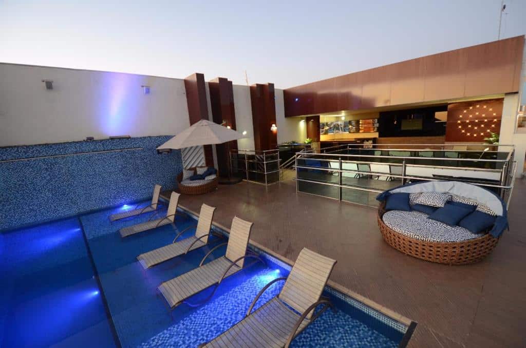 Área externa do Oscar Hotel Executive. Do lado esquerdo uma piscina com cadeiras de tomar sol dentro, do lado direito dois sofás, uma grade com cadeiras.