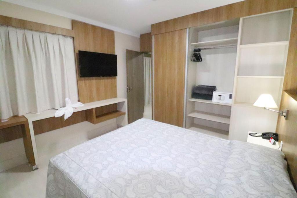 Quarto do Piazza Acqua Park. Uma cama de casal do lado direito com um armário no fundo com cofre, cobertor e cabide. De frente para a cama uma estante, uma cortina e uma televisão. Foto para ilustrar post sobre airbnb em Caldas Novas.