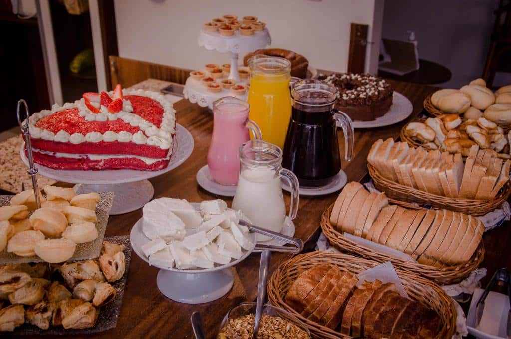 Mesa do café da manhã da Pousada Lanai Gramado. Cestas com pães, bolos, salgados e pães. No meio jarras com suco e leite.