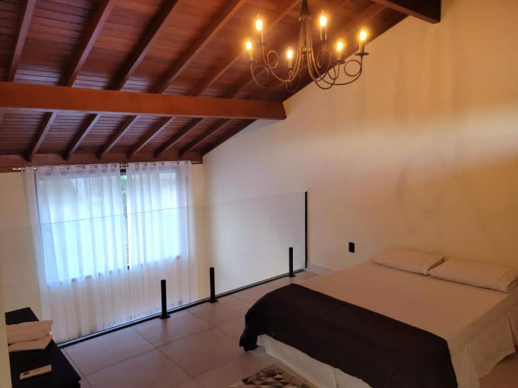 Quarto do BrotasLoft no segundo andar com uma cama de casal com dois travesseiros e uma colcha. O teto é de madeira e a divisão do segundo andar para o primeiro é um vidro.