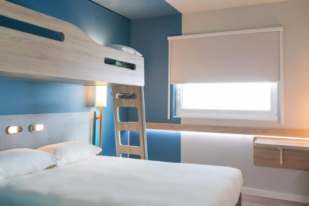 Foto de um quarto no ibis budget Geneve Palexpo Aeroport, para ilustrar o post de hotéis em Genebra. Há uma cama de casal e uma beliche em cima, de solteiro. O quarto também possui uma janela com cortinas.