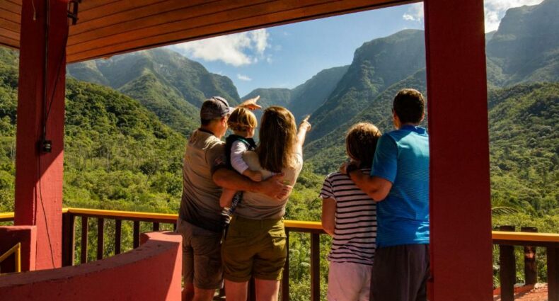 Uma família com dois adultos e uma criança no colo está no lado esquerdo e um adulto está ao lado de outra criança no lado direito. Todos estão de costas para a foto apontando para o cânion que estão vendo a frente. Imagem para ilustrar o post pousadas em Aparados da Serra.