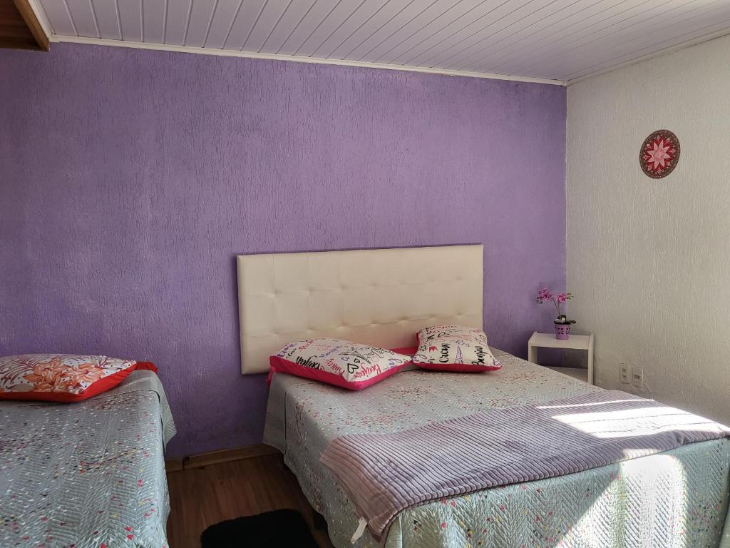 Quarto no Residência Cardoso. Há uma cama de casal na direita e uma de solteiro ao seu lado, à esquerda. A parede atrás é roxa. Representa o post sobre airbnb em Canela.
