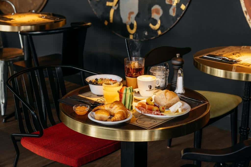 Foto no restaurante do Ruby Claire Hotel Geneva. As paredes, piso e móveis são escuros. Uma mesa está no centro com variedades de café da manhã, como croissants, cereais, frutas, sucos, etc.