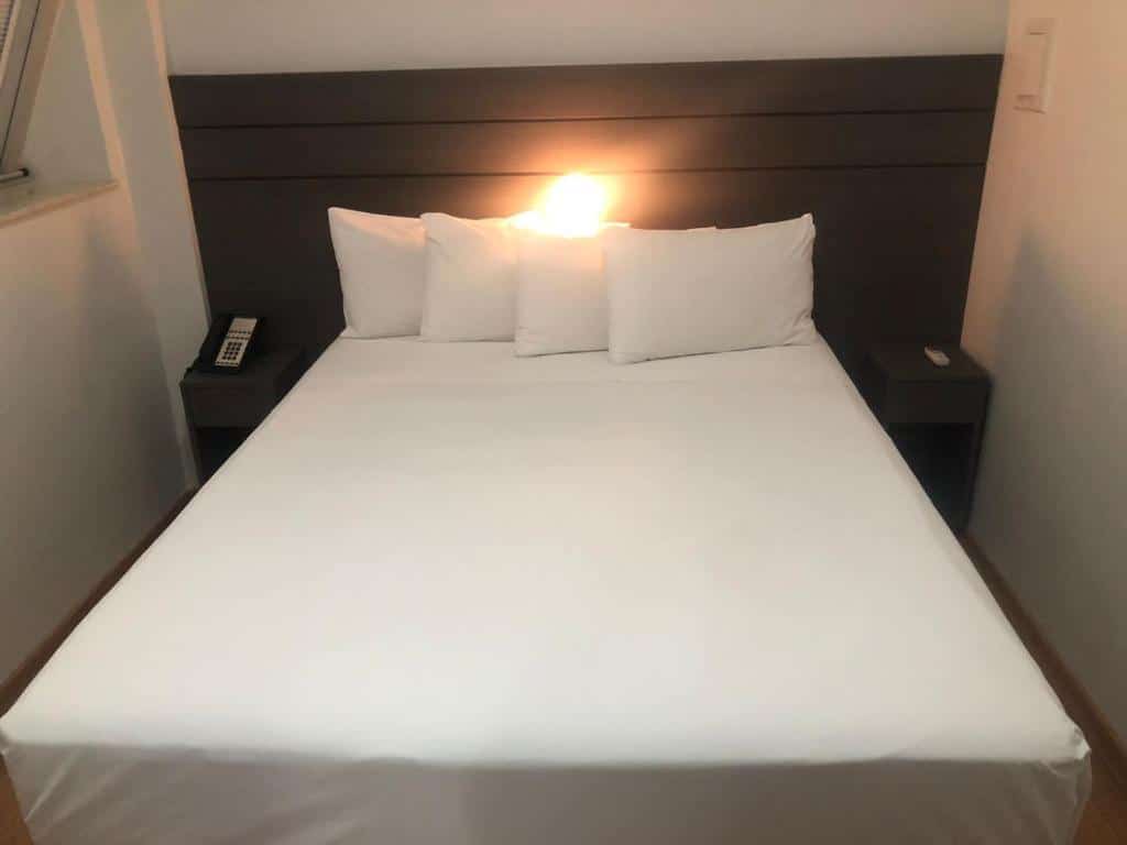 Uma cama box de casal com lençóis e travesseiros brancos no San Diego Apto 808.