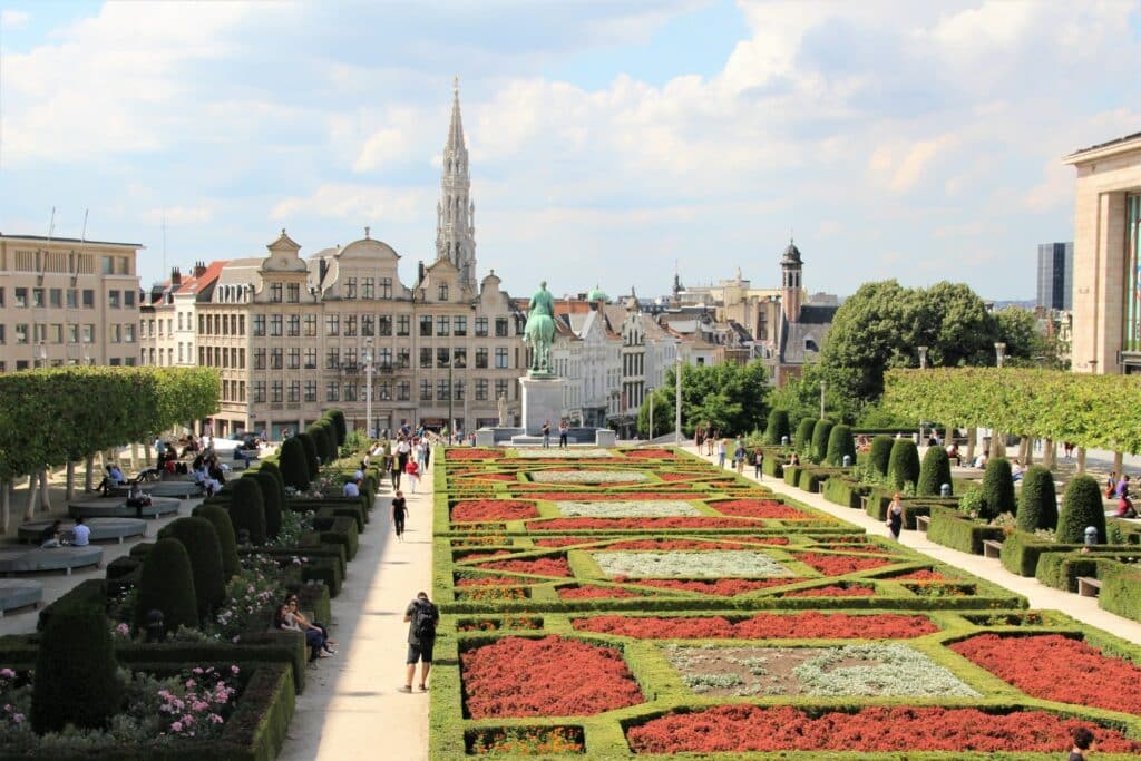 Um amplo jardim a céu aberto com plantas ornamentais com pessoas passeando, ao redor há prédios históricas, para representar seguro viagem Bélgica