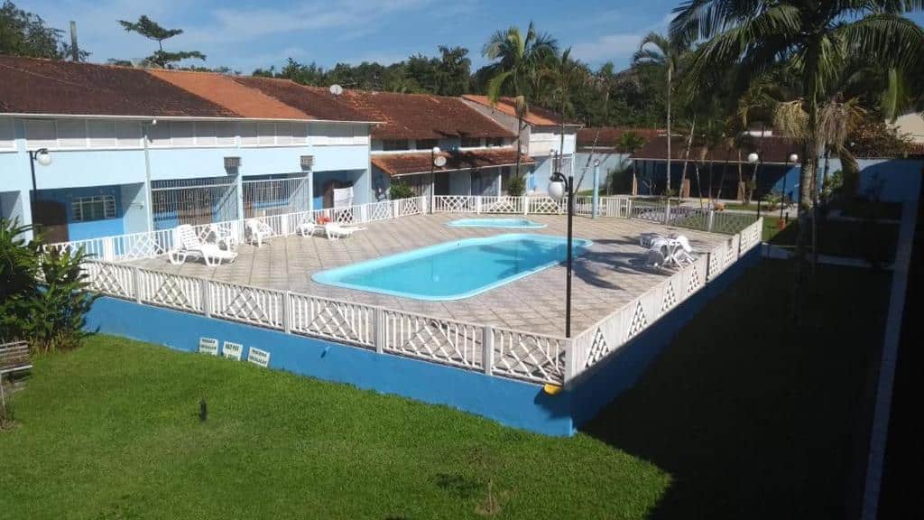 Área externa do SOBRADO VILLAGE UBATUBA PER-AÇU. Uma piscina no centro, ao redor cadeiras de tomar sol. grade e um jardim.