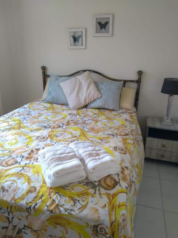 Quarto do Solar Lisboa. Uma cama de casal com almofadas e toalhas, do lado direito uma cômoda com abajur. Foto para ilustrar post sobre airbnb em Balneário Camboriú.