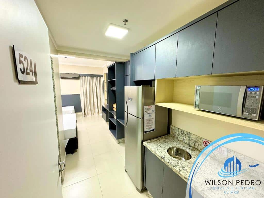 Mini cozinha do Spazzio diRoma. Uma pia com micro-ondas, armários e geladeira do lado direito. No fundo os armários e as camas do quarto.