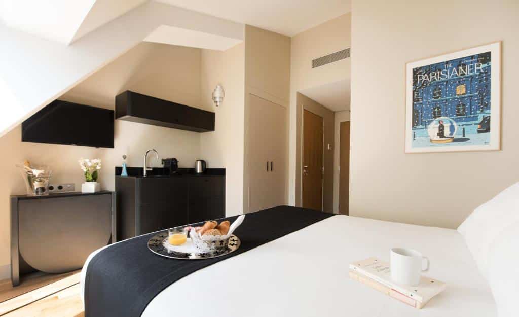Visão da cozinha das Suites & Hôtel Helzear Etoile, um dos hotéis com cozinha em Paris, a partir da cama. Há fogão, pia, cafeteira e chaleira na parede repleta de bancadas e armários.
