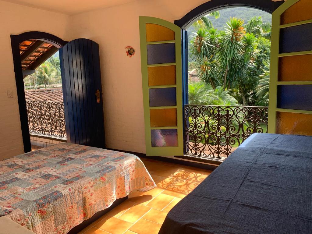 Quarto do Vivencie nossa energia. Do lado direito uma cômoda, do lado esquerdo uma cama de casal, de frente uma porta aberta da sacada e do lado esquerdo a porta do quarto. Foto para ilustrar post sobre airbnb em Perequê Mirim.